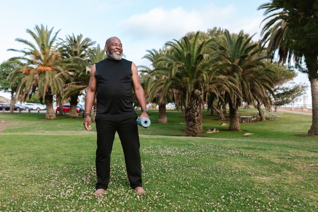 Elderly African American man doing yoga with a mat in a sunny park.
