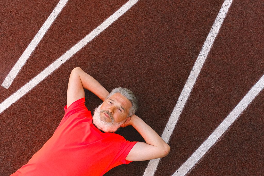 From above of calm elderly female with gray hair lying and relaxing on racetrack in stadium