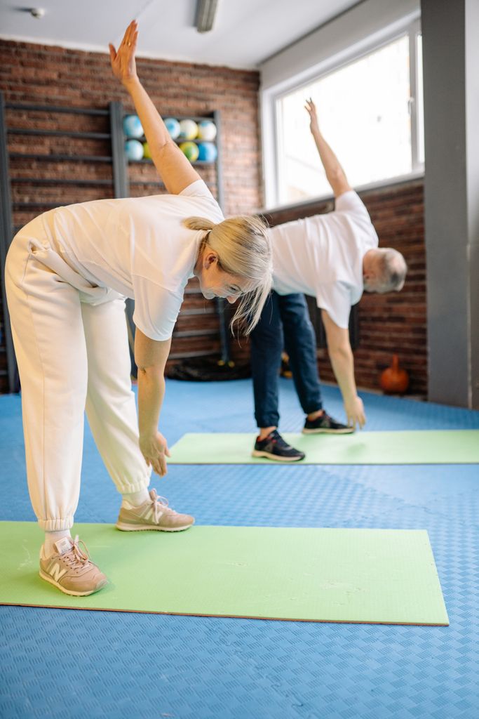 Senior adults stretch on mats in a fitness gym, promoting a healthy lifestyle.