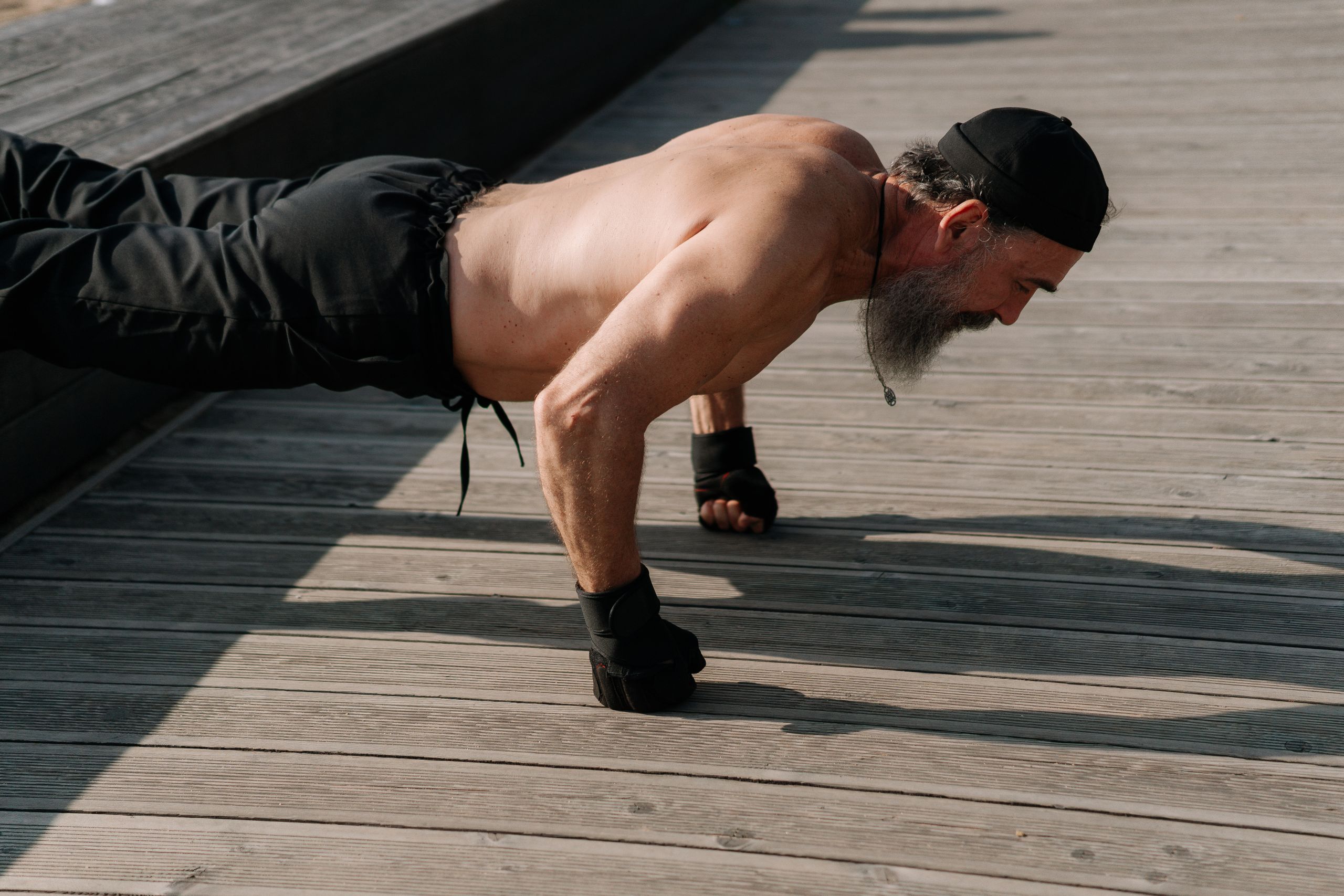 Men’s Health After 40 Senior man with a beard exercising outdoors, performing push-ups on a wooden deck.